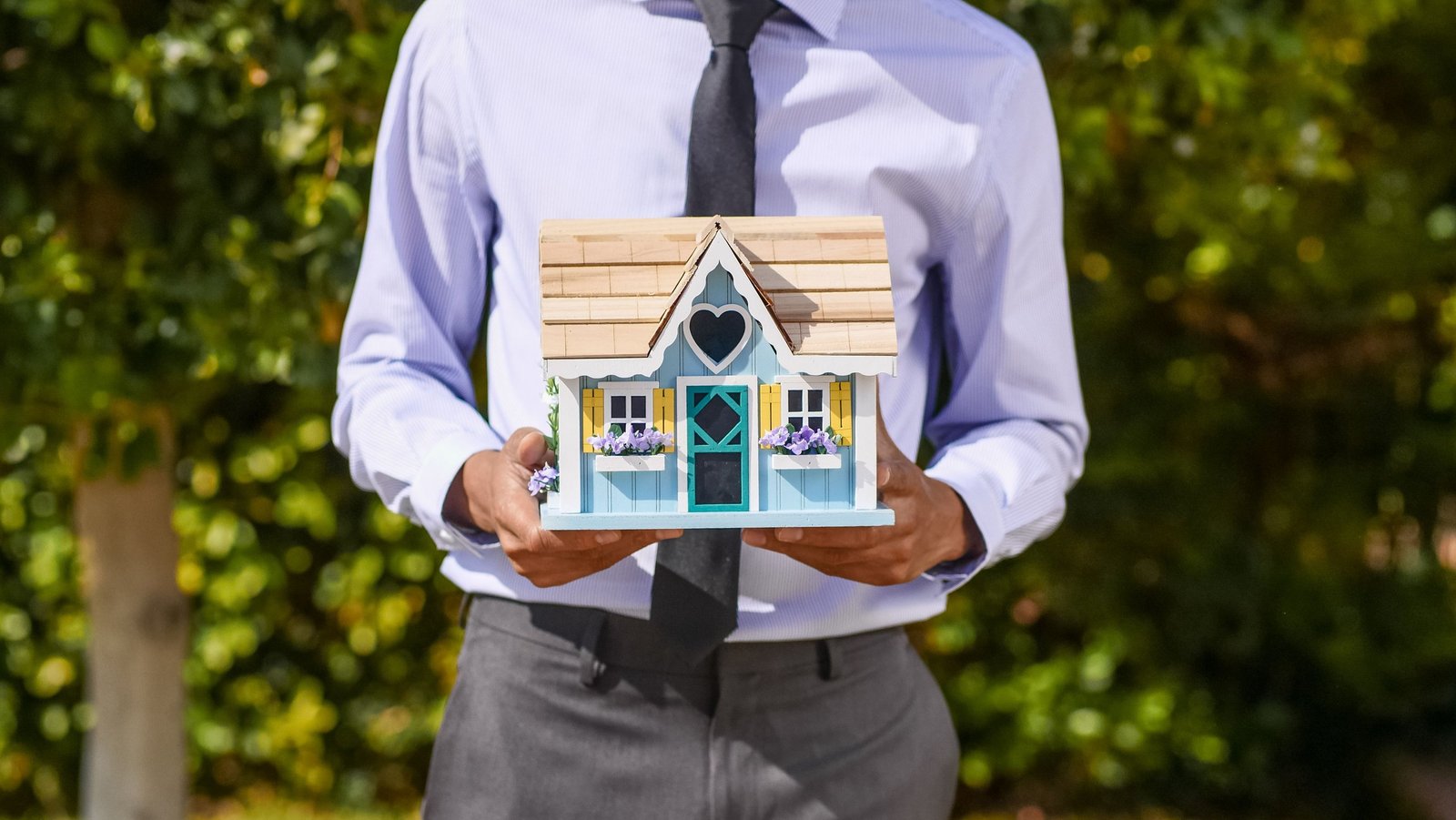 Real estate professional holding a model house outdoors